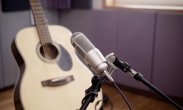Shure SM81 microphone facing an acoustic guitar in a diffused natural-light live room